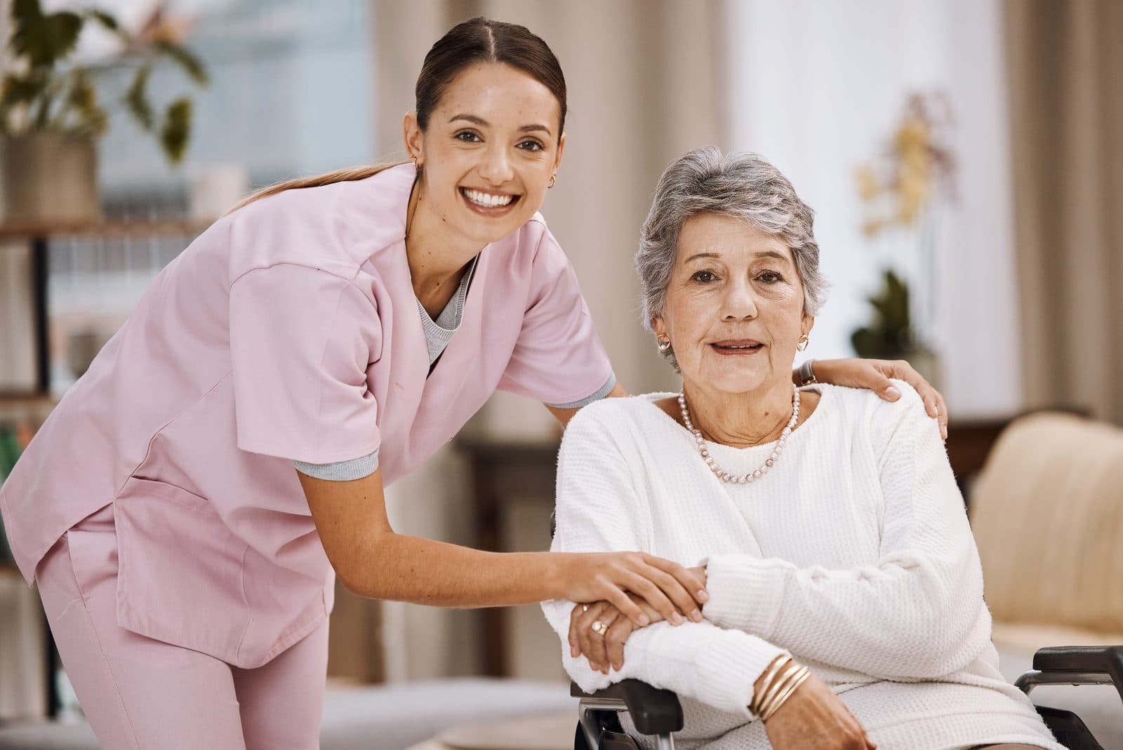 Cuidadora sonriendo junto a una señora mayor en silla de ruedas