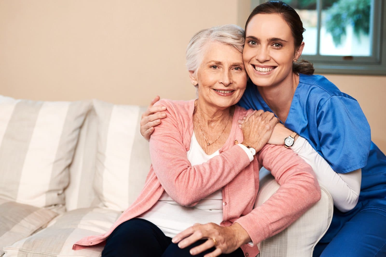 Cuidadora y señora mayor abrazadas y sonriendo en el sofá