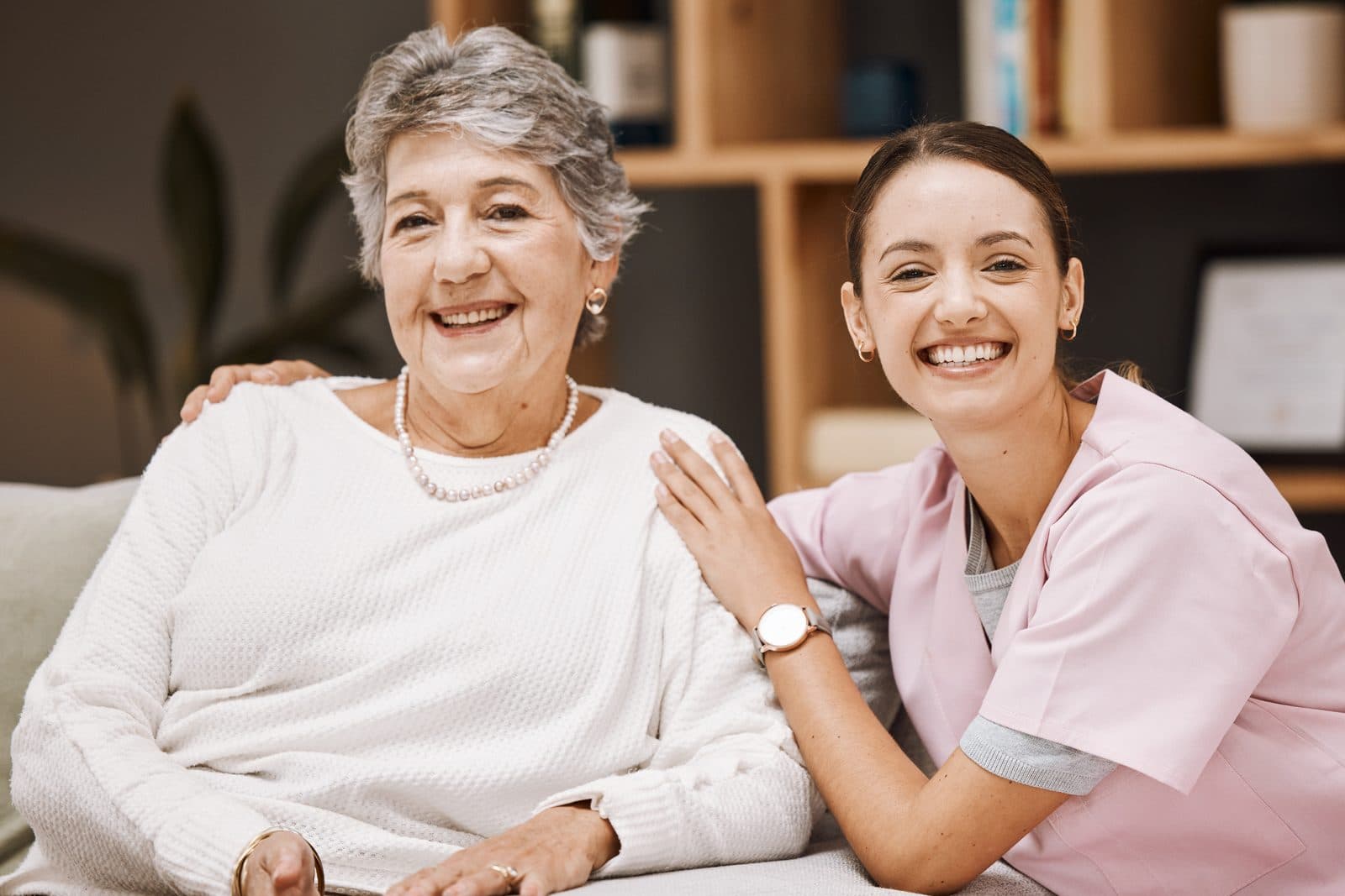 Cuidadora y señora mayor sonriendo sentadas juntas en el sofá