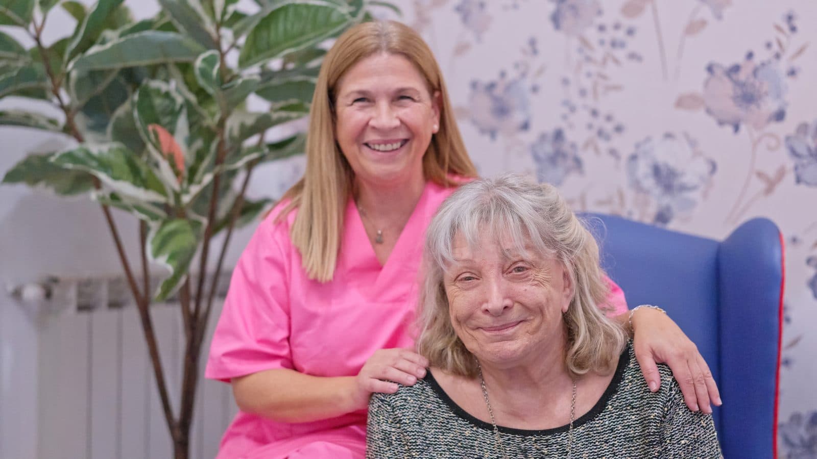 Cuidadora y señora mayor sonriendo juntas en el salón
