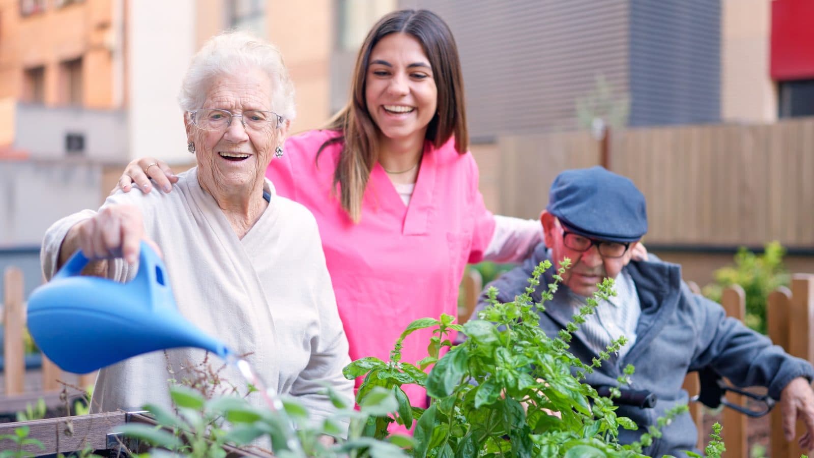 Señora mayor regando las plantas acompañada de su cuidadora