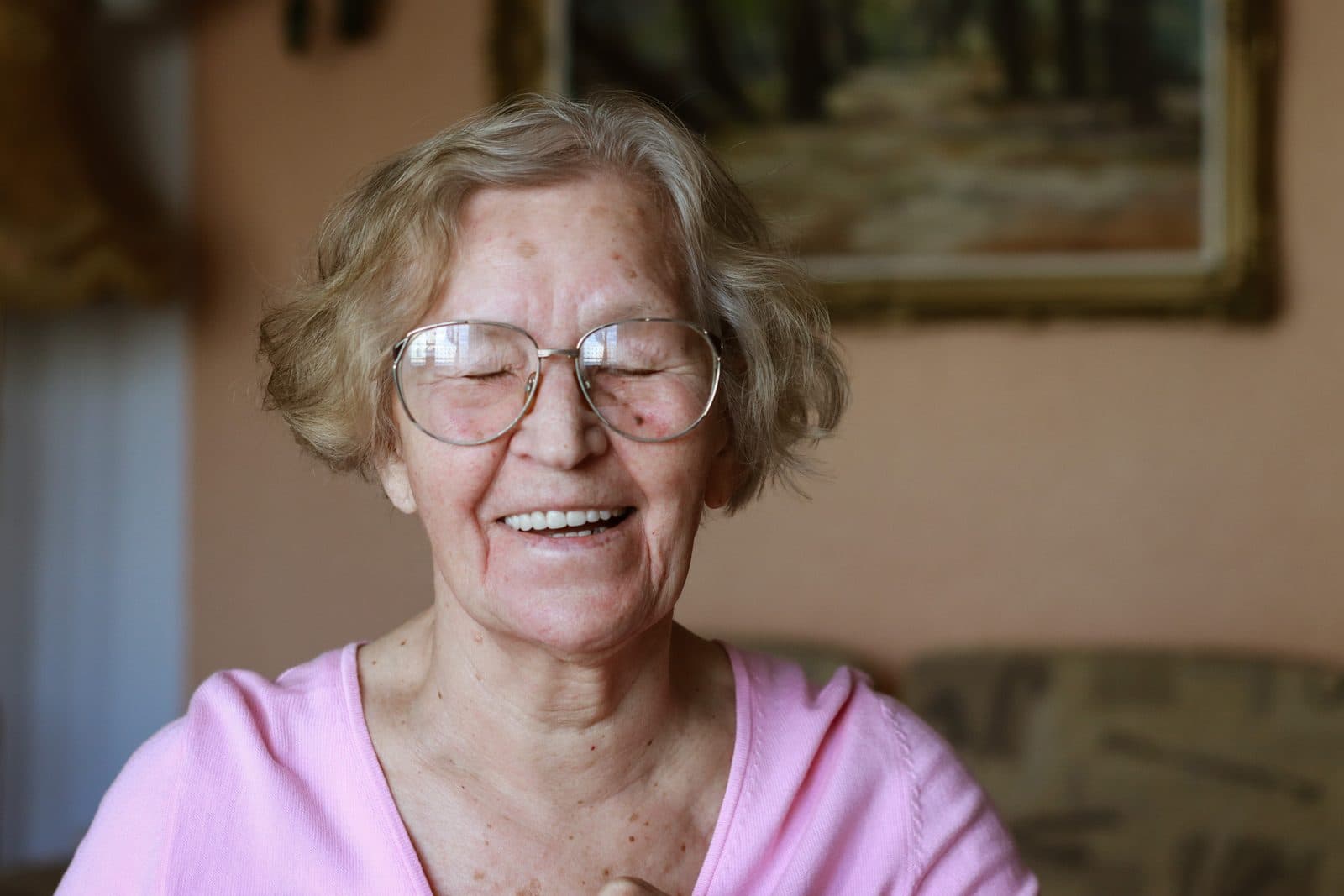 Señora mayor con gafas sonriendo en el salón de su casa