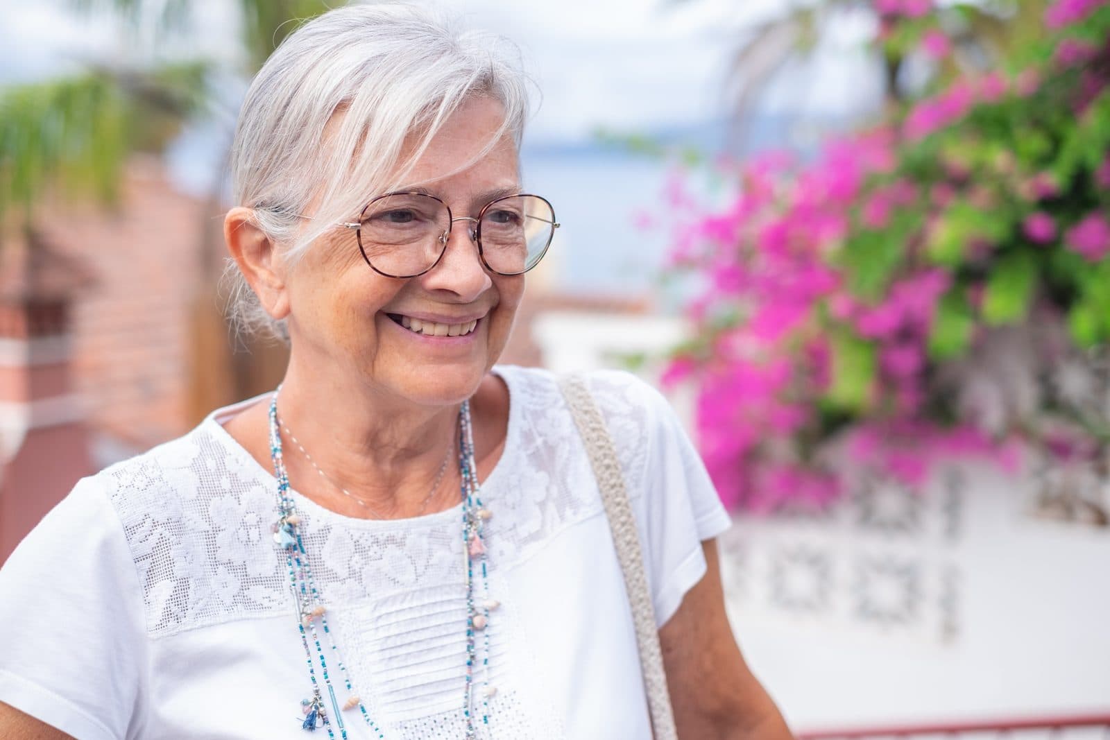 Señora mayor con gafas sonriendo en una calle con buganvillas