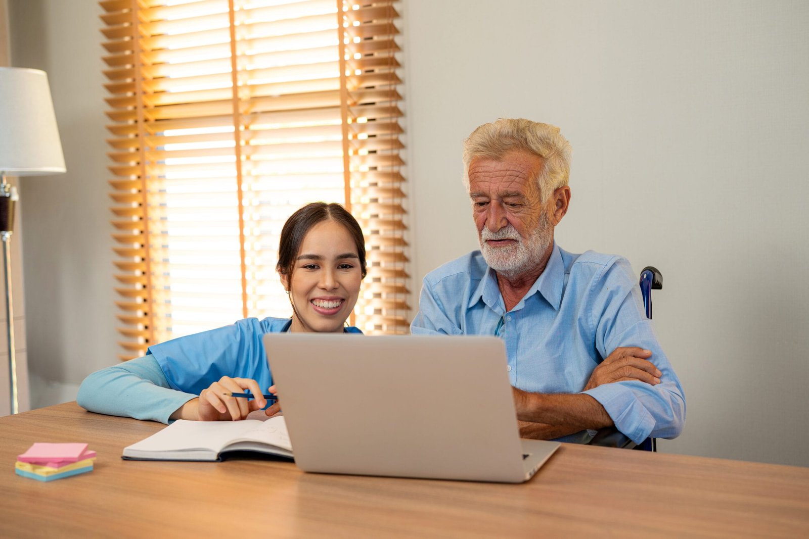 Profesional ayudando a un mayor en silla de ruedas a usar un portátil